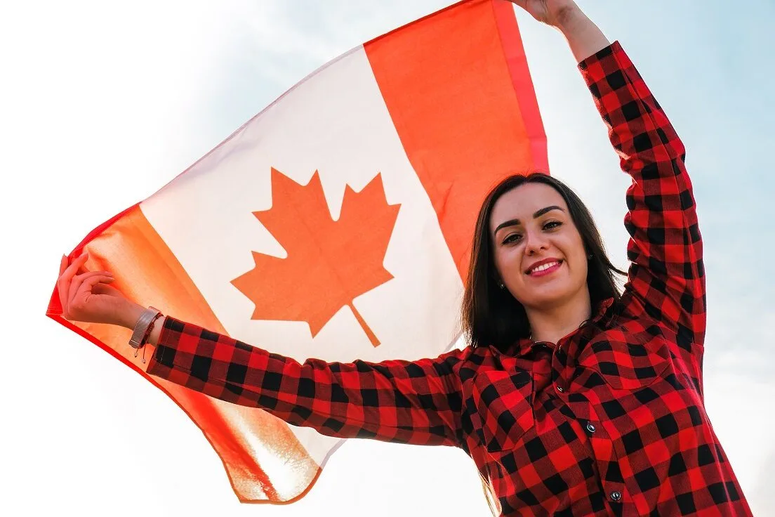 Mulher jovem segurando a bandeira do Canadá, vestindo camisa xadrez vermelha, simbolizando orgulho nacional e oportunidades para imigrantes no país.